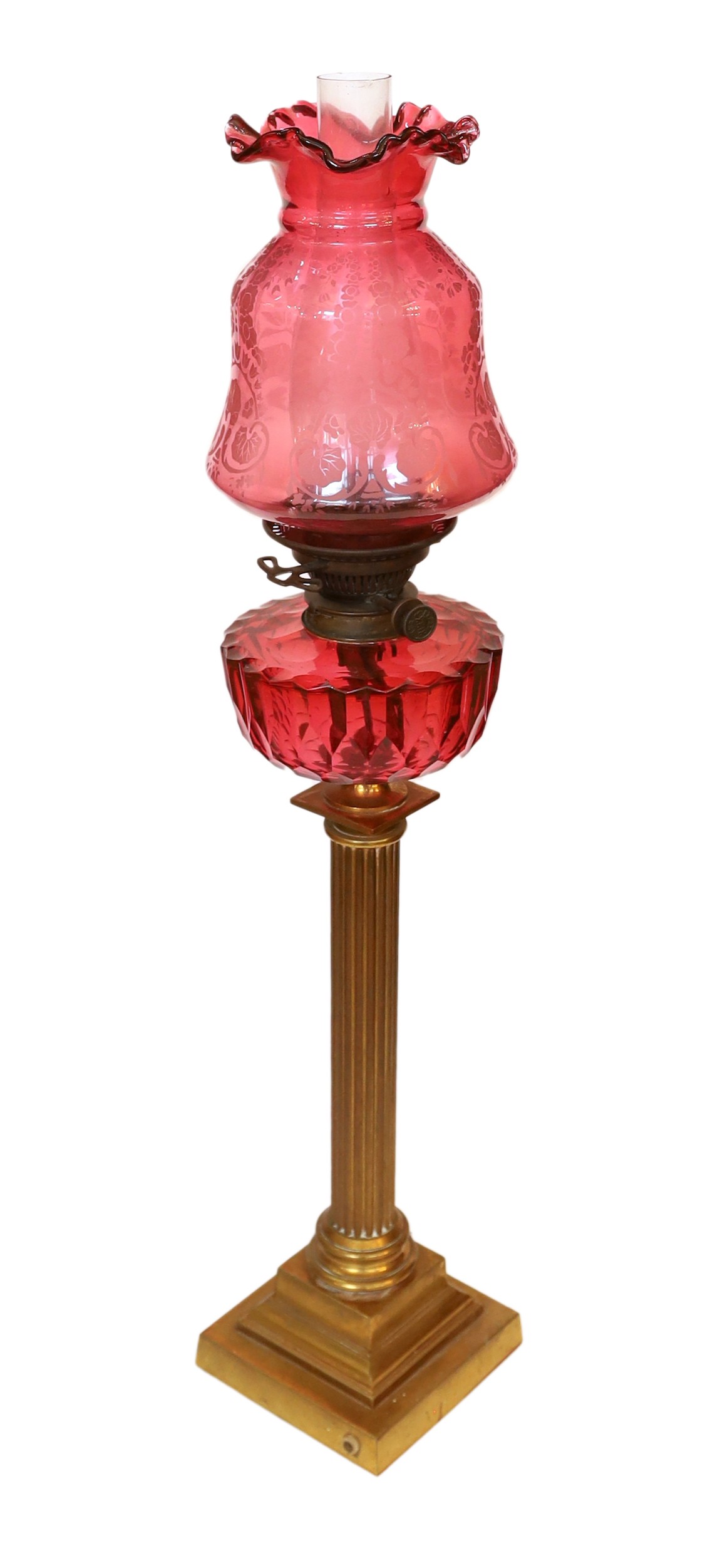 A Victorian lacquered brass fluted column oil lamp with cut ruby glass reservoir, Hinks No2 mechanism, etched cranberry glass shade and flue, height overall 86cm